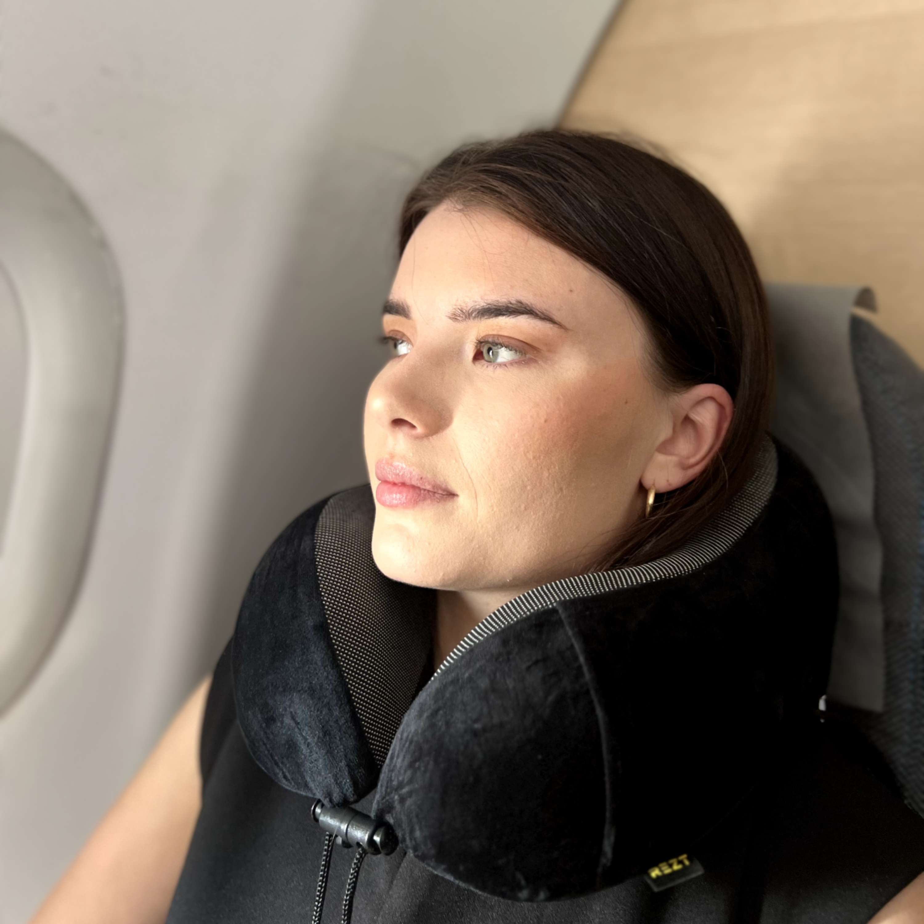 En kvinne hviler komfortabelt på et flysete, med hodet støttet av en REZT reisepute.