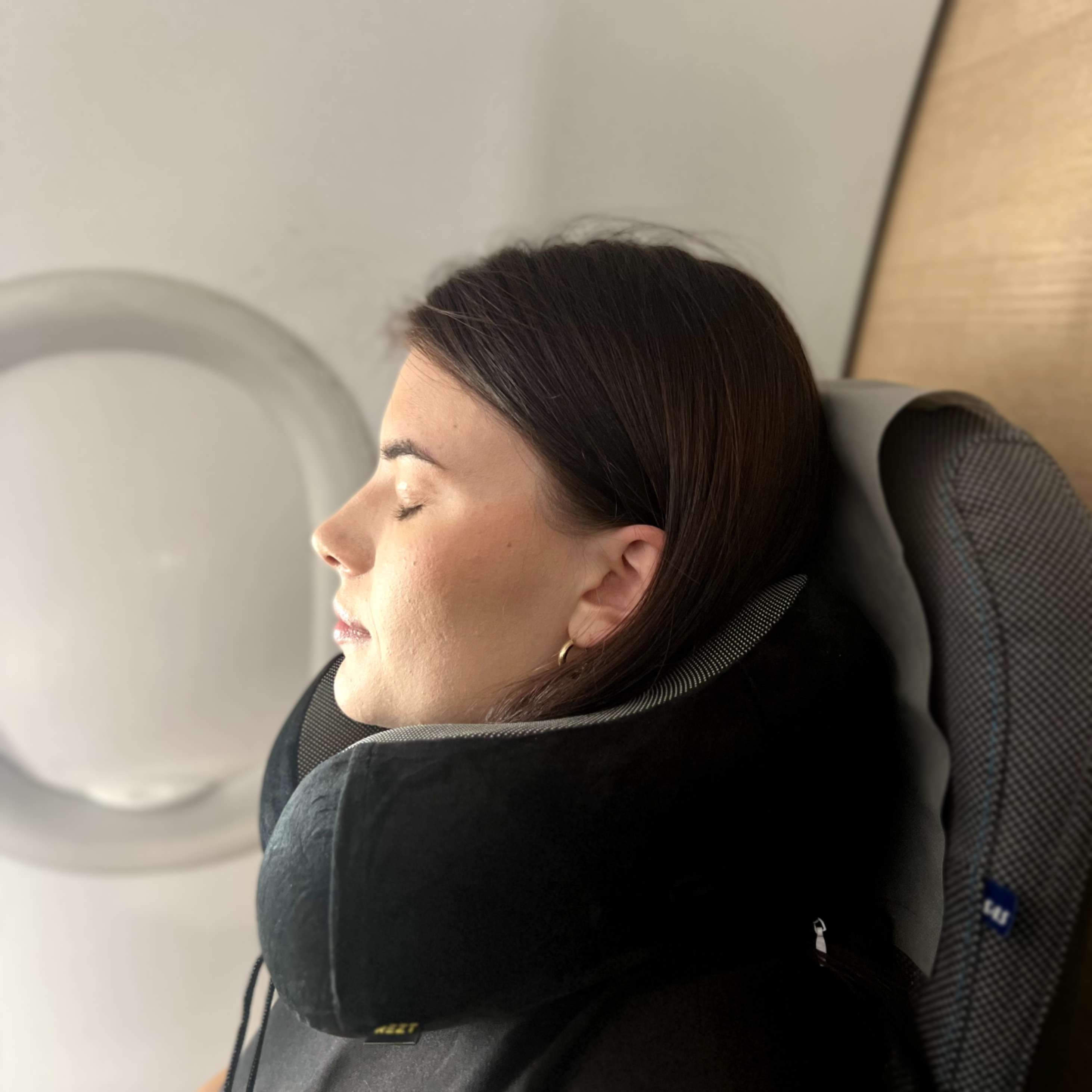En kvinne slapper av i et flysete med en støttende REZT reisepute